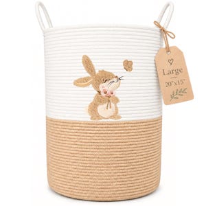 Op de afbeelding: Een tweekleurige cilindrische mand van katoentouw met een wit bovenste en beige onderste gedeelte. Een geborduurd bruin konijn met roze bloemen staat centraal op het witte deel. Een beige label vermeldt Large 20"x15".
