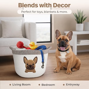 Op de afbeelding: Een witte touwmand met een bruin-witte gestreepte rand en een Franse bulldog-applicatie. De mand bevat een rood balspeelgoed, een gele badeend en een blauwe riem. Een Franse bulldog zit naast de mand. De tekst luidt "Blends with Decor".