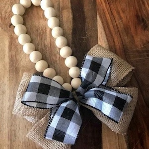 May include: A wooden bead garland with a black and white buffalo check bow. The garland is made of natural wood beads and the bow is tied with burlap ribbon.