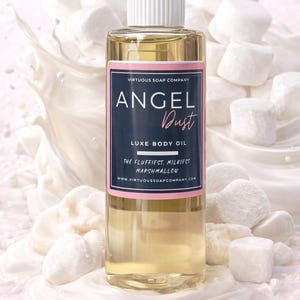 May include: A clear bottle of "Angel Dust" Luxe Body Oil with a white cap and a navy blue and pink label. The label includes the text "The fluffiest, milkiest marshmallow". The background features white marshmallows and a white liquid splash.