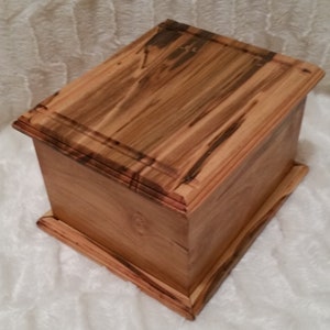 May include: A wooden box with a natural wood finish. The box has a raised lid with a decorative border. The box is made of solid wood and has a rustic look.