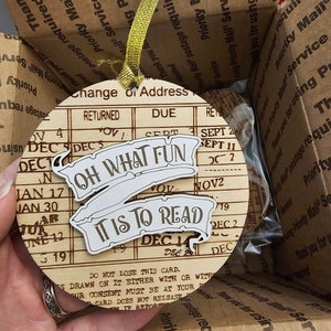 Peut inclure: Une d&eacute;coration en bois en forme de carte de changement d'adresse vintage. La d&eacute;coration pr&eacute;sente le texte "Oh What Fun It Is To Read" dans une banni&egrave;re.