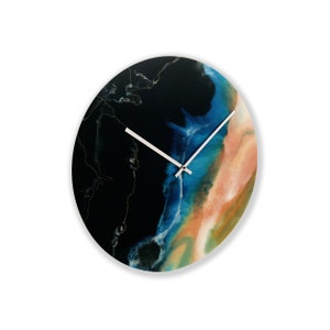 Puede incluir: Un reloj redondo con un diseño abstracto negro, azul y naranja. Las manecillas del reloj son plateadas.