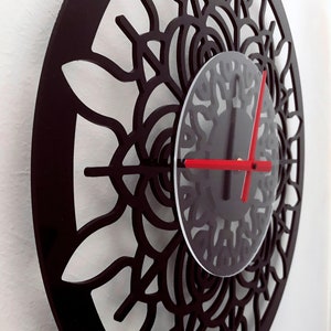 Puede incluir: Un reloj negro con un diseño de mandala y agujas rojas. La esfera del reloj es un círculo transparente con un diseño de mandala negro.