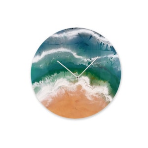 Puede incluir: Un reloj redondo con una escena de playa. La esfera del reloj presenta un océano azul y verde con olas blancas rompiendo en una playa de arena.