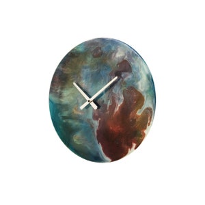 Puede incluir: Un reloj redondo con una esfera blanca y agujas negras. La esfera del reloj está hecha de resina y tiene un patrón de remolino de colores azul, verde y marrón.