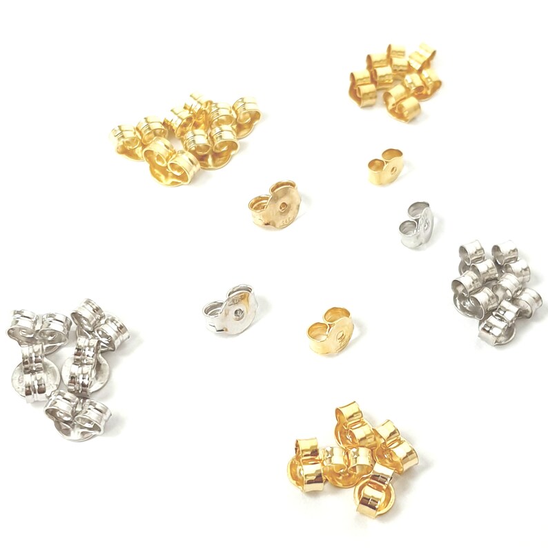 May include: Assortment of earring backs in gold and silver tones. The backs are made of metal and have a butterfly closure. There are multiple piles of earring backs in different colors.