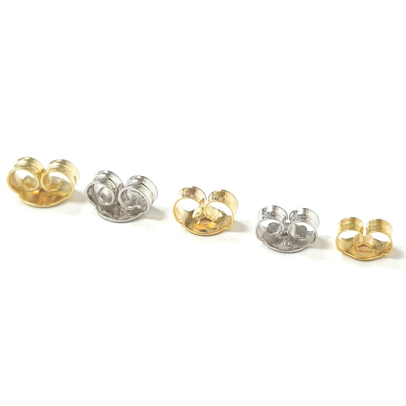 May include: Four earring backs in different finishes: gold, silver, and two shades of gold. The backs are designed to secure earrings with a post.