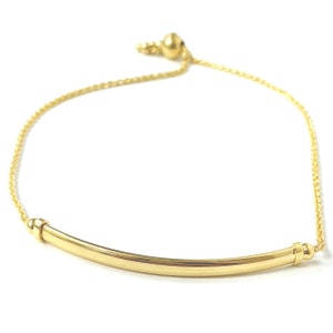 May include: A gold chain bracelet with a curved bar charm. The bracelet is adjustable with a sliding bead.
