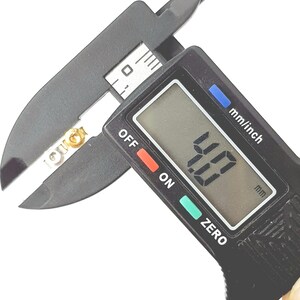 May include: A black digital caliper measuring 4.00 mm. The caliper has a black display with white numbers, a red "OFF" button, a green "ON" button, and a green "ZERO" button. The caliper is measuring a small, gold-colored object.
