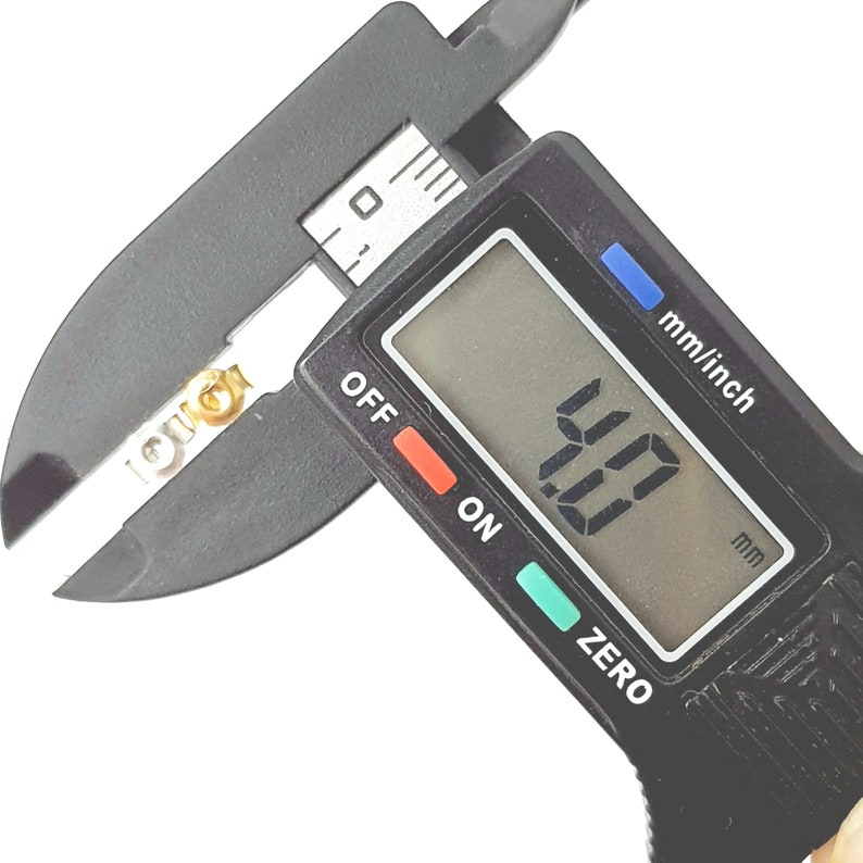 May include: A black digital caliper measuring 4.00 mm. The caliper has a black display with white numbers, a red "OFF" button, a green "ON" button, and a green "ZERO" button. The caliper is measuring a small, gold-colored object.