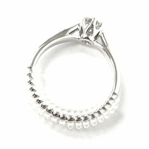 May include: A silver ring with a single round diamond set in a prong setting. The band is made of a series of small, round beads.