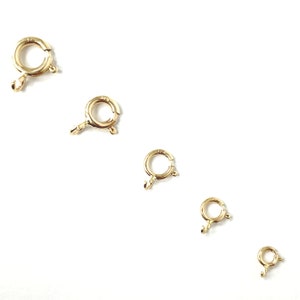 May include: Five gold-toned jump rings of different sizes. The rings are all round and have a small opening on one side. They are commonly used for jewelry making.