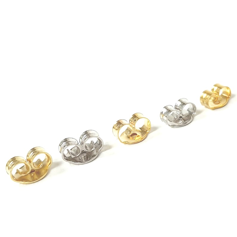 May include: Four earring backs in different finishes: gold, silver, rose gold, and white gold. The backs are designed to secure earrings in place.