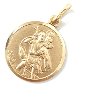 May include: A gold-colored pendant featuring a detailed relief of Saint Christopher carrying a child. The round pendant has a loop for a chain and is set against a white background. The pendant is likely made of gold.