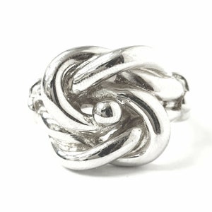 May include: A silver knot ring with a smooth, polished finish. The ring is designed with a complex knot pattern and a small, round bead in the center.