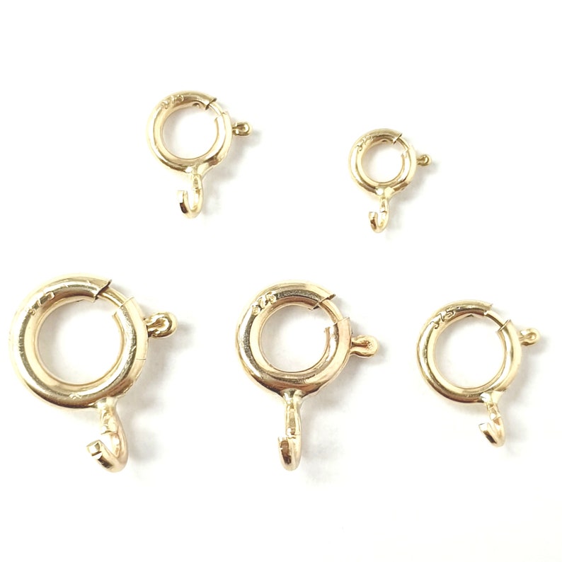 May include: Five gold jump rings of different sizes. The jump rings are round and have a hook closure.