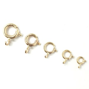 May include: Five gold-toned jump rings of varying sizes. The rings are open and have a small hook on one side.