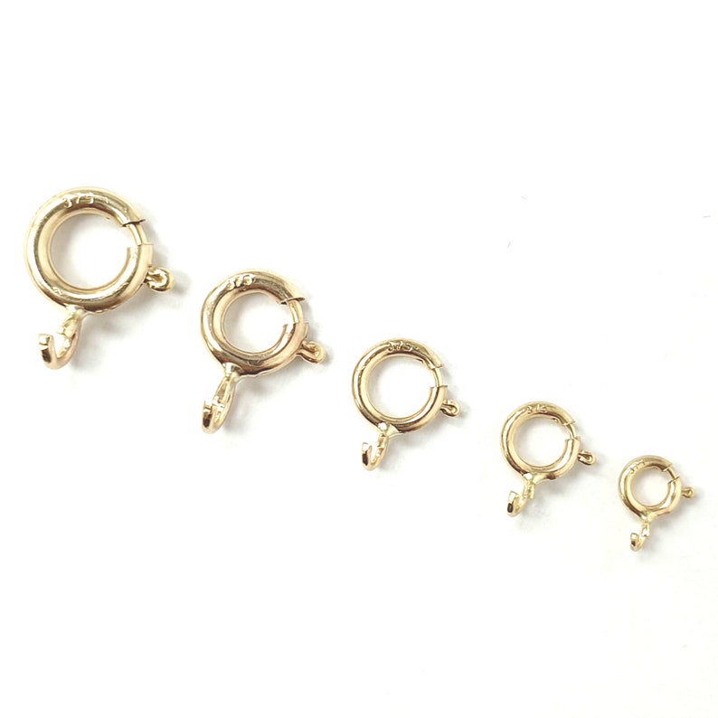 May include: Five gold-toned jump rings of varying sizes. The rings are open and have a small hook on one side.
