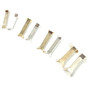 May include: Six metal watch band sizing tools with different markings. The tools are silver and gold in colour. The markings on the tools include "9ct No. 5", "Sil No. 5", "Silver No. 7", "9ct No. 7", "9ct No. 10", and "9ct No."