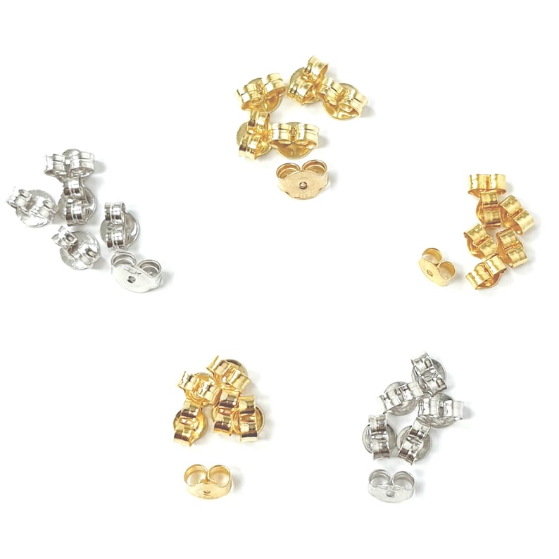 May include: A close-up of three piles of earring backs. The piles are arranged in a circle. The earring backs are made of metal and are available in gold, silver, and rose gold.