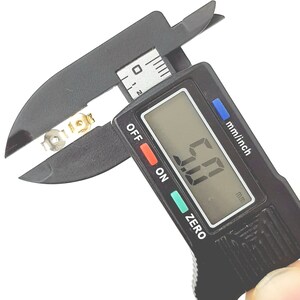 May include: A black digital caliper with a silver metal object being measured. The caliper display reads "0.00" mm.