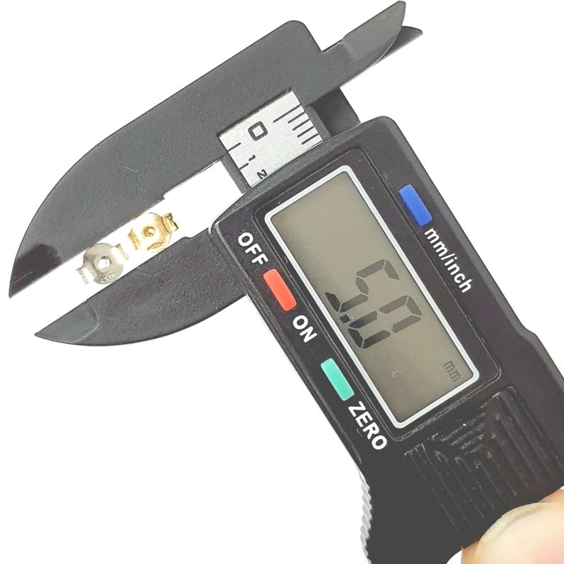 May include: A black digital caliper with a silver metal object being measured. The caliper display reads "0.00" mm.