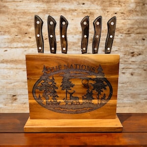 May include: Wooden knife holder with a rustic design. The holder features a carved scene of a forest with trees, a deer, and the text "The Nation's". Six knives are displayed in the holder.