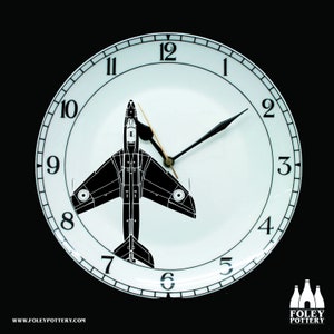 May include: A white ceramic clock plate with black numbers and hands. A black silhouette of a jet plane is in the center of the plate.