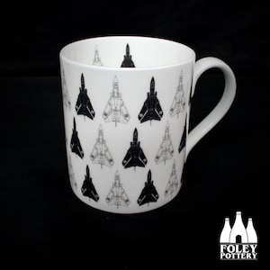 May include: A white ceramic mug with a black and white pattern of fighter jets. The mug has a handle and is printed with the text "FOLEY POTTERY".
