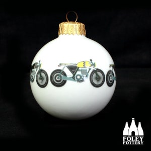 May include: White Christmas bauble featuring a black and yellow motorcycle design. The bauble has a gold top.