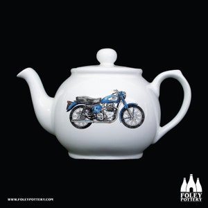 Könnte beinhalten: Weiße Keramik-Teekanne mit einem blauen und schwarzen Motorrad-Design. Das Motorrad ist im klassischen Stil mit einem runden Scheinwerfer und einem Einzelsitz.