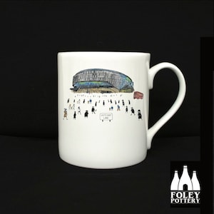 Puede incluir: Taza de cerámica blanca con una ilustración en blanco y negro de un estadio con personas y un autobús rojo. El texto "White Hart Lane" está en un cartel en la ilustración. La taza está hecha por Foley Pottery.