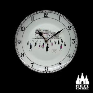 May include: White ceramic clock with black numbers and hands. The clock face features a black and white illustration of a stadium with people walking around it. The text "LIPSON PARK" is visible on the clock face. The clock is made by FOLEY POTTERY.