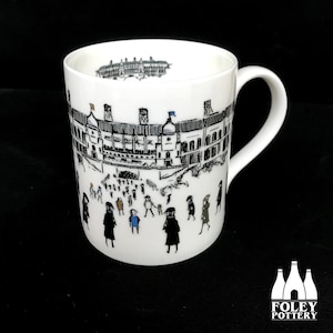 May include: White ceramic mug with a black and white illustration of a building with people in front of it. The mug has a black handle and the words "FOLEY POTTERY" are printed on the bottom.