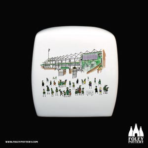 Puede incluir: Jarrón de cerámica blanca con una ilustración dibujada a mano de una escena de estadio con personas. El estadio tiene detalles en verde y blanco. El jarrón tiene una forma rectangular redondeada. El texto "FRANKLIN GARDENS" es visible.