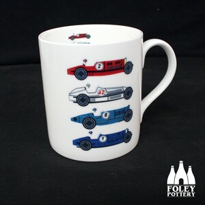 Puede incluir: Taza de cerámica blanca con un diseño de cinco coches de carreras vintage en rojo, blanco y azul. Los coches están numerados 1, 2, 8 y 42.