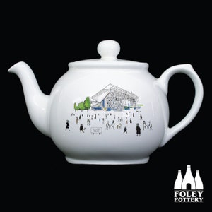 May include: White ceramic teapot with a black and white illustration of a stadium and people walking around it. The text "Elland Road" is visible on the teapot.