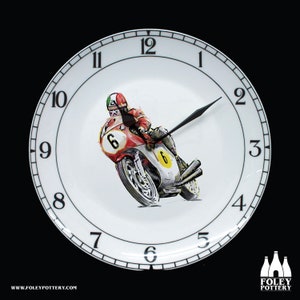 Könnte beinhalten: Eine weiße Keramik-Uhr mit schwarzen Zahlen und Zeigern. Das Zifferblatt der Uhr zeigt eine farbenfrohe Illustration eines Motorradrennfahrers auf einem rot-weißen Motorrad.