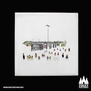 Könnte beinhalten: Eine weiße Keramikfliese mit einer Schwarzweißillustration eines Stadions mit Menschen, die herumlaufen. Der Text "The Environment is Tough" steht auf einem Schild im Bild.