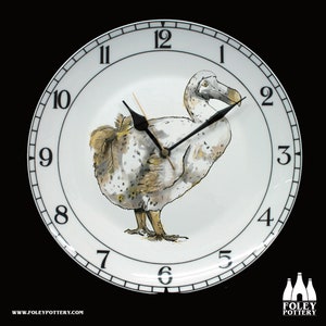 May include: A white ceramic clock with black Roman numeral markings and black hands. The clock face features a hand-painted illustration of a dodo bird. The clock is made by Foley Pottery.