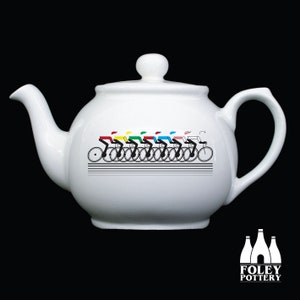 May include: White ceramic teapot featuring a black and white design of cyclists in a line. The cyclists are wearing different coloured jerseys, including red, yellow, green, blue, and white. The teapot has a black handle and spout.