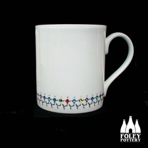 May include: White ceramic mug with a curved handle. The base of the mug features a repeating pattern of stick figures in various colours, including blue, red, and yellow. The Foley Pottery logo is in the bottom right corner.