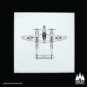 Puede incluir: Un dibujo en blanco y negro de un avión de combate P-38 Lightning con estrellas rojas, blancas y azules en las alas. El avión se ve desde arriba.