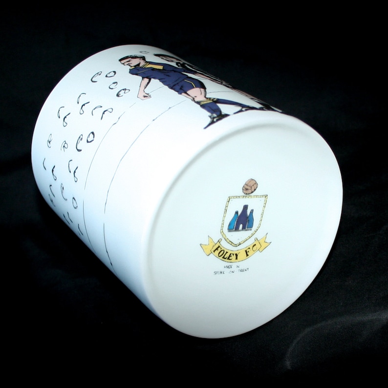May include: White ceramic mug with a black and white illustration of soccer players on one side and a crest with the text "Foley FC Made in Stoke-on-Trent" on the other side.
