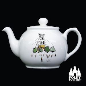 Puede incluir: Tetera de cerámica blanca con una ilustración en negro, verde y amarillo de una estructura minera, árboles y personas. La tetera tiene un pico curvo, un cuerpo redondeado y un asa de bucle. El texto "HEM HEATH" es visible.