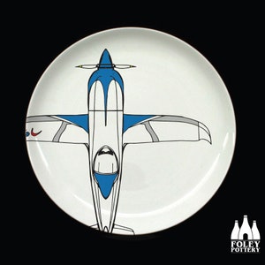 May include: A white ceramic plate with a blue and white airplane design. The airplane is facing down with the wings spread out. The plate is a part of a collection of plates with different airplane designs.