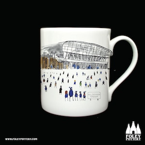 Könnte beinhalten: Weiße Keramiktasse mit einer Schwarz-Weiß-Illustration eines Stadions und einer Menschenmenge. Die Tasse hat einen gebogenen Henkel und die Worte "Hill Dickinson Stadium" sind auf einem Schild zu sehen.