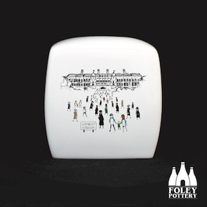 May include: White ceramic storage jar with a black and white illustration of Wembley Stadium and people walking towards it. The text "Wembley Stadium" is printed on a sign in the image.