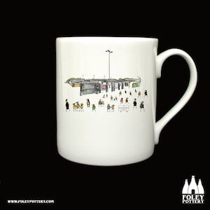 Könnte beinhalten: Weiße Keramiktasse mit einer Schwarzweißillustration eines Schulgebäudes und Kindern. Der Text "Enrolment" steht auf einem Schild in der Illustration.